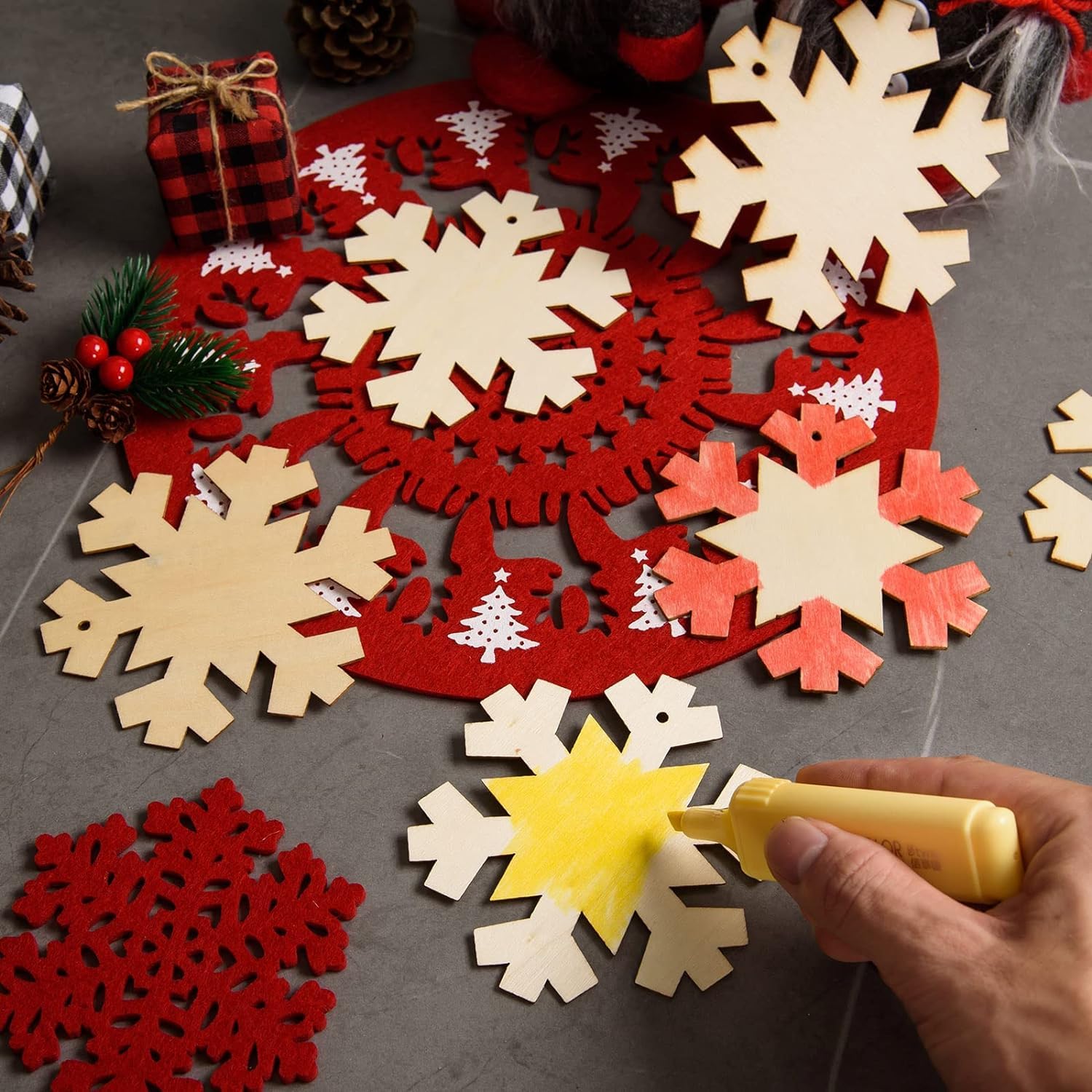 Decorative snowflake cutouts in red, white, and yellow on a gray surface with a hand holding a glue gun.