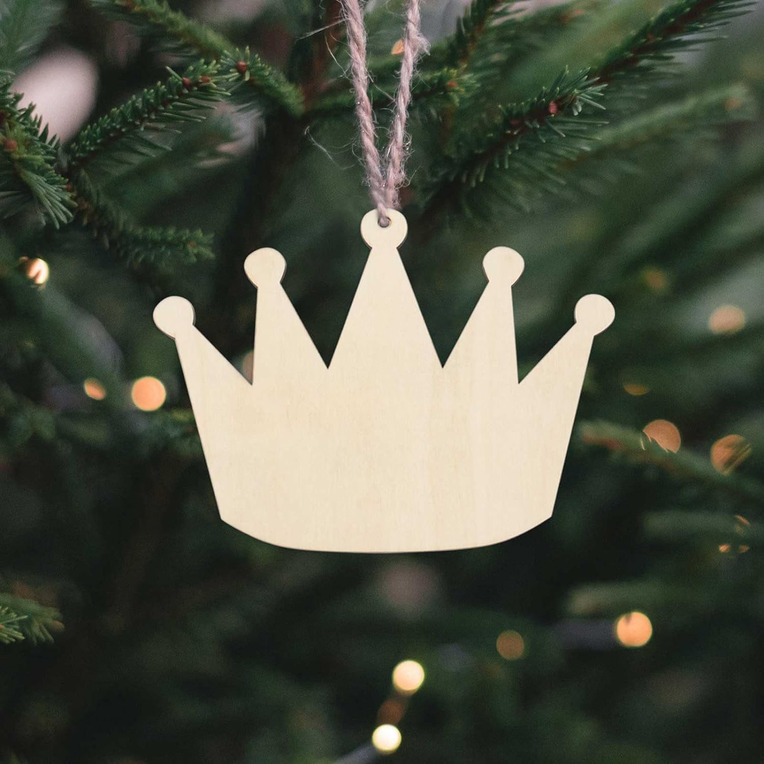 Wooden crown ornament hanging on a Christmas tree with blurred lights in the background