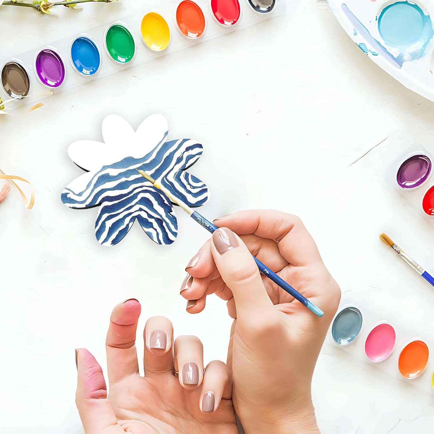 Person painting a blue and white butterfly with watercolors on a white surface.