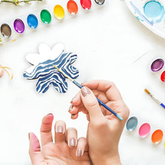 Person painting a blue and white butterfly with watercolors on a white surface.
