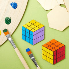 Two Rubik's cubes on a green surface with paintbrushes and paint.