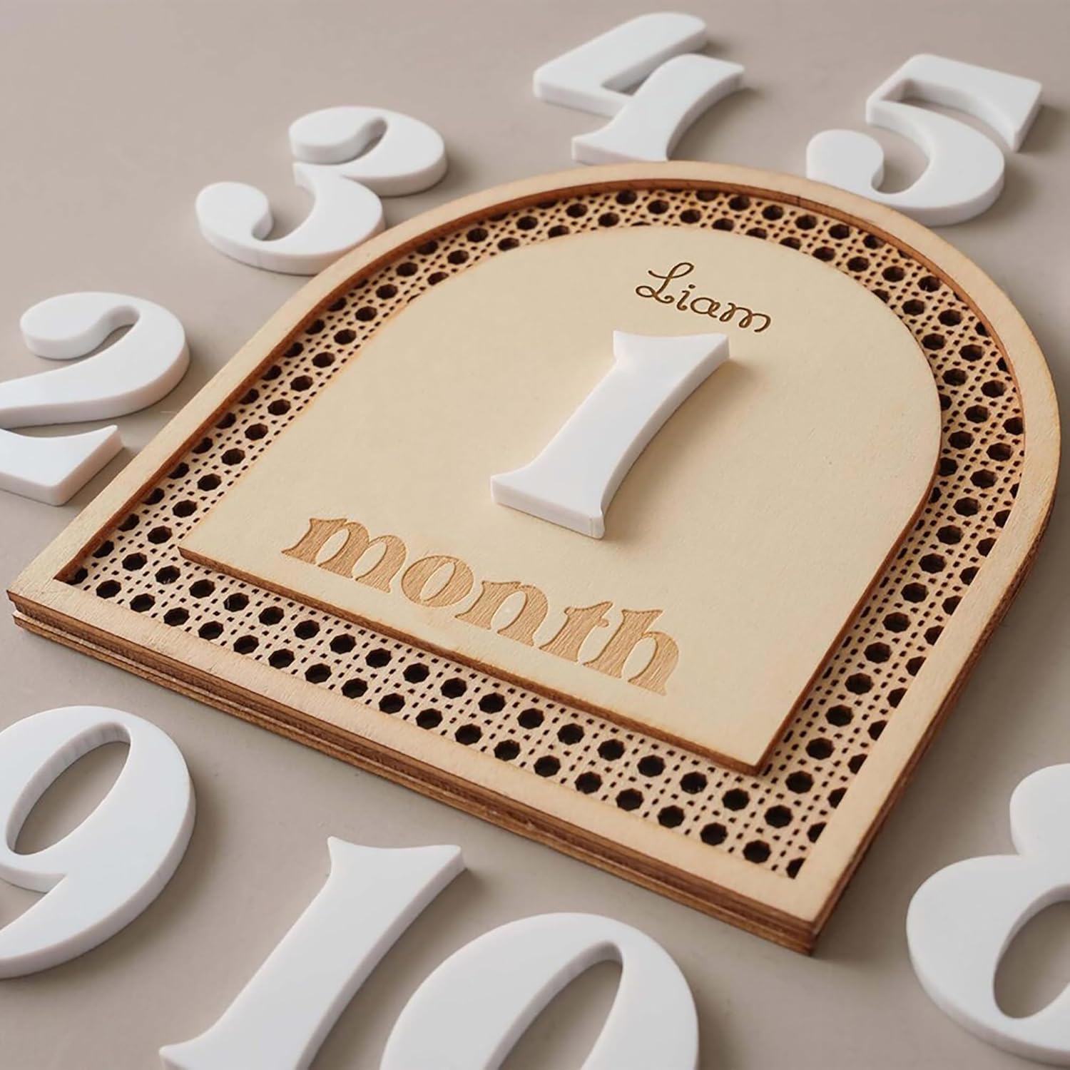 Wooden plaque with 'Liam' and '1 month' engraved, surrounded by white numbers on a beige background