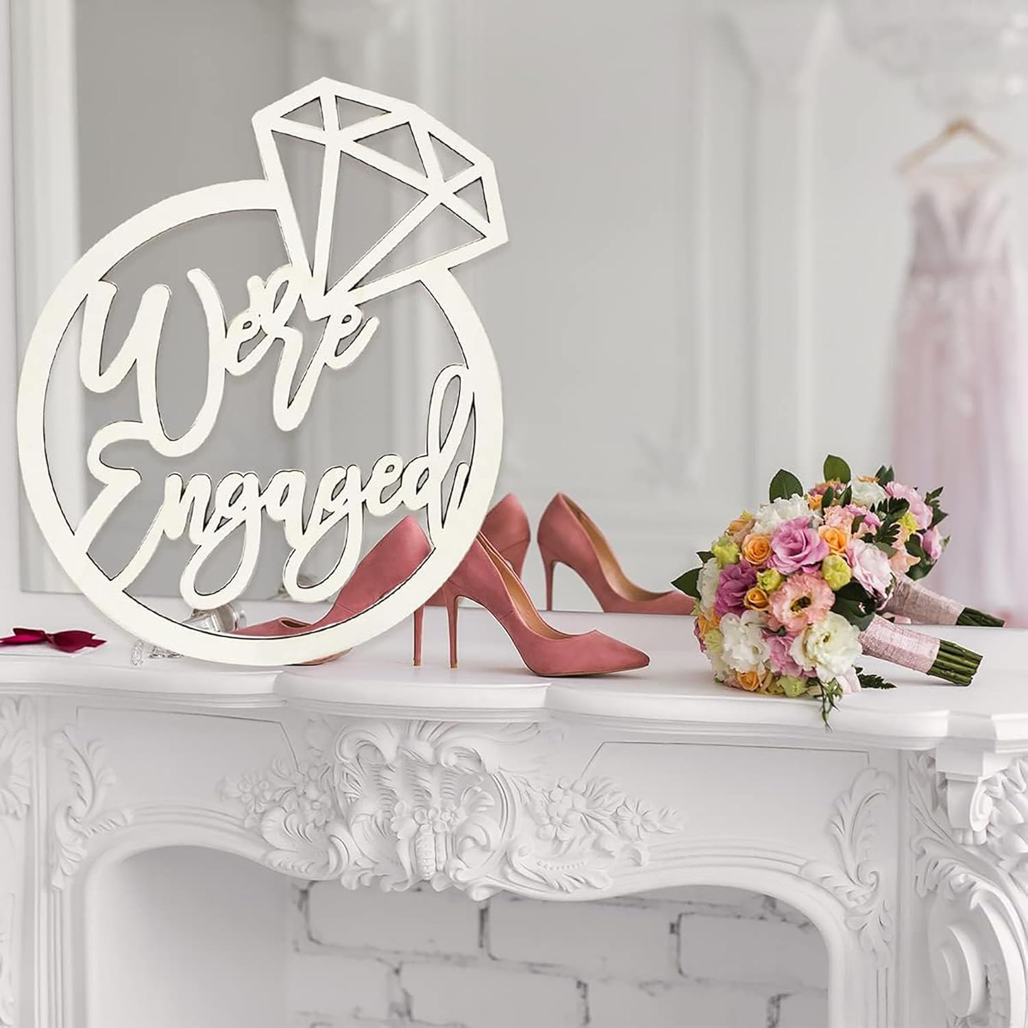 Decorative sign with 'We're Engaged' text on a white surface with high heels and flowers.