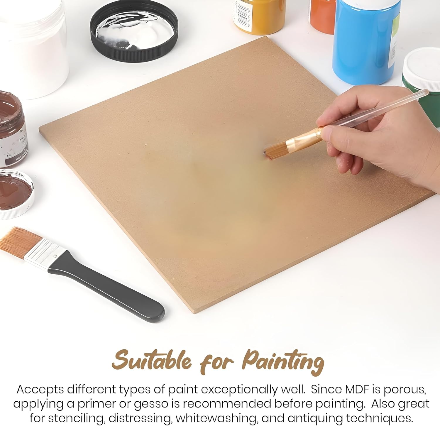 Person painting a wooden board with a brush, surrounded by paint containers and tools on a white surface.