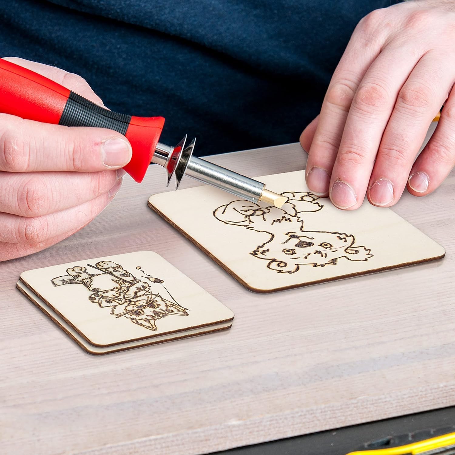 Person using a tool to cut out laser-cut wooden coasters with designs on a wooden surface.