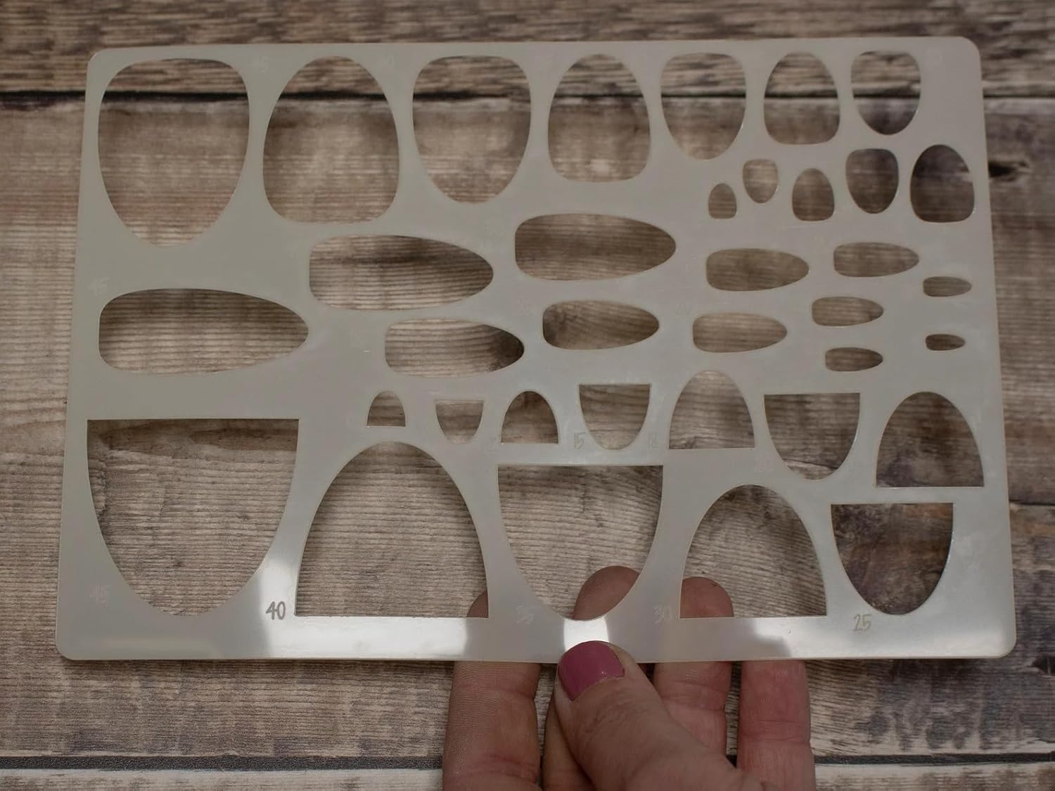 Metal template with cut-out shapes held by a hand on a wooden surface