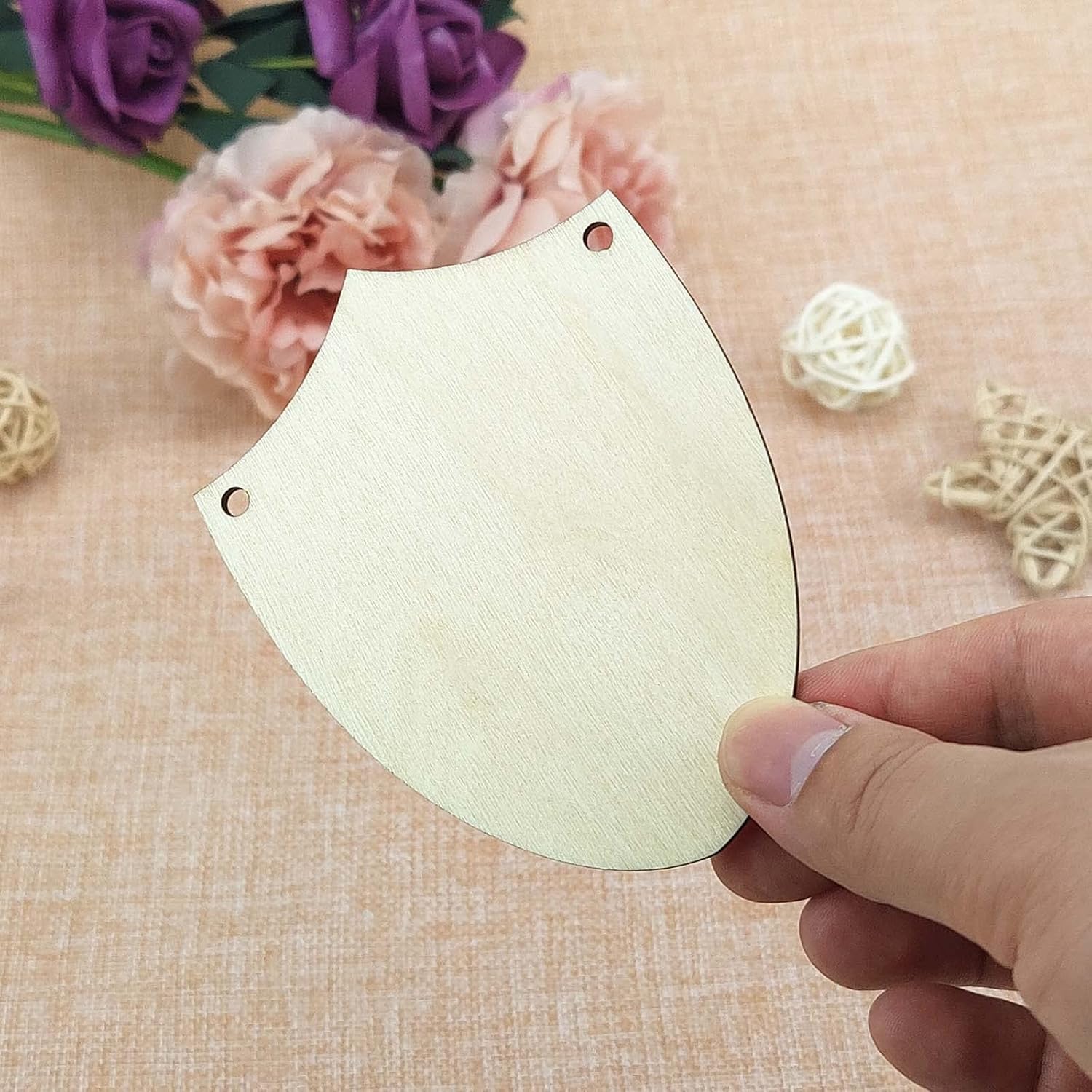 Hand holding a beige paper cutout with floral decorations in the background
