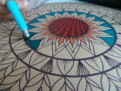 Hand holding a stylus over a mandala design on a textured surface
