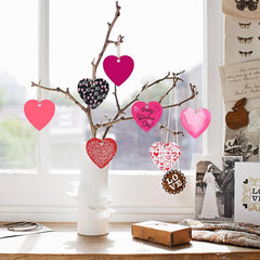 Decorative branch with heart-shaped ornaments in a vase on a table.