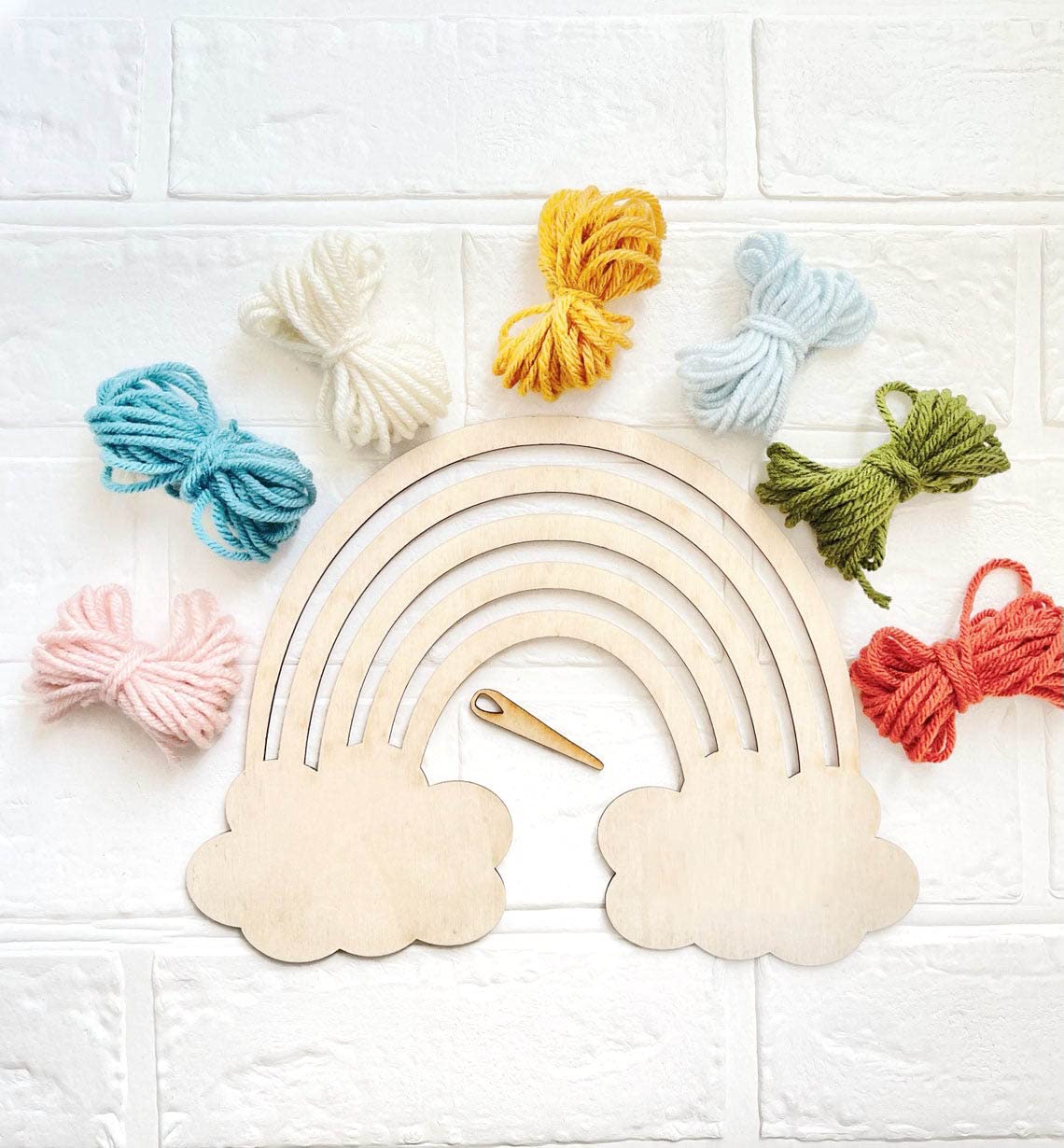 Wooden rainbow with yarn balls on a white tiled background