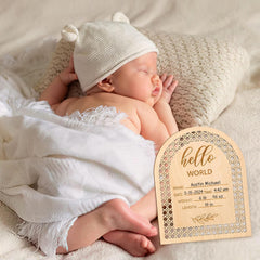 Newborn baby wrapped in white with a 'hello world' sign next to it