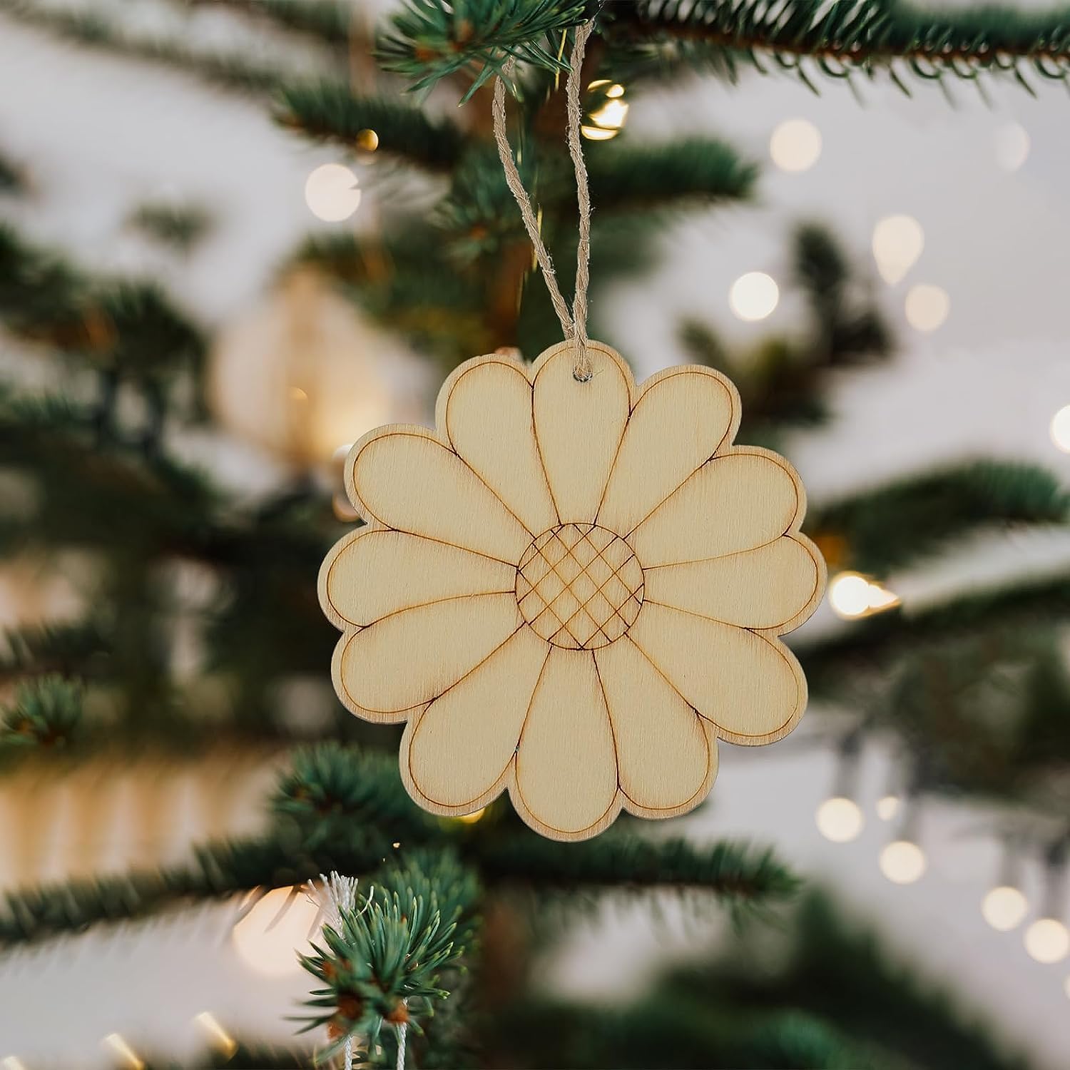 Wooden daisy ornament hanging on a Christmas tree with blurred lights in the background