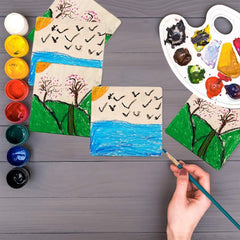 Children's artwork with trees, birds, and water on a wooden surface, accompanied by paint supplies.
