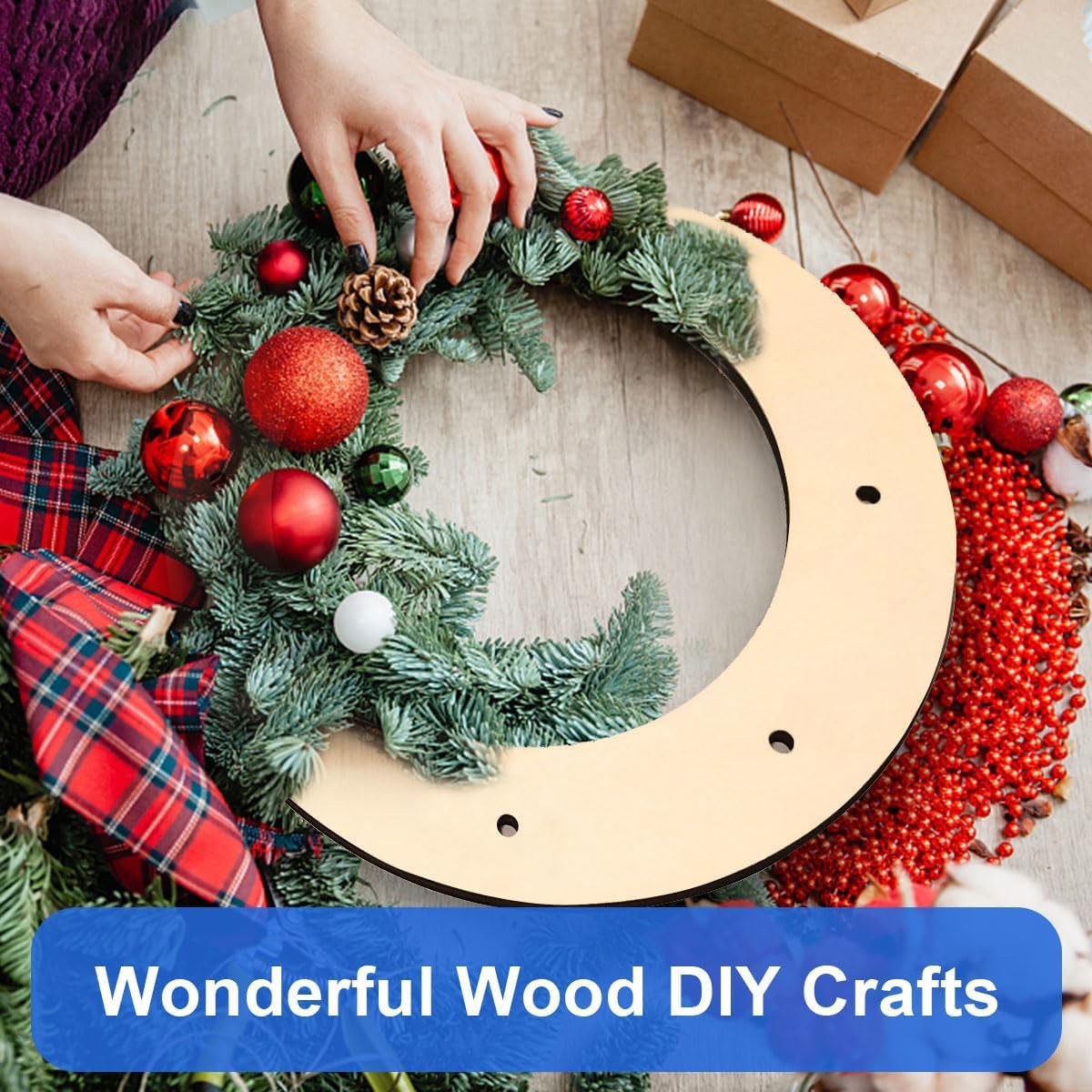 Person decorating a Christmas wreath with red ornaments on a wooden surface.