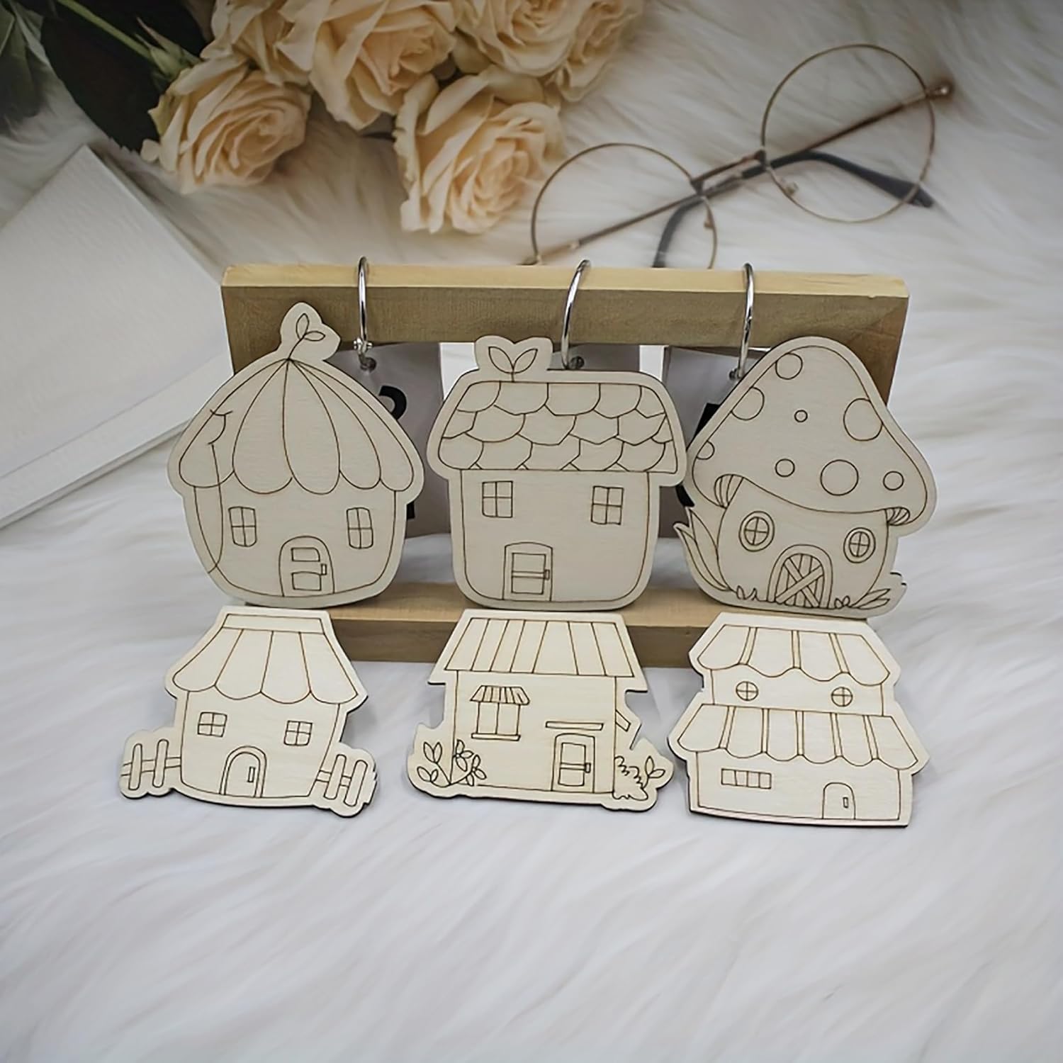 Set of house-shaped wooden keychains on a stand with flowers and glasses in the background.
