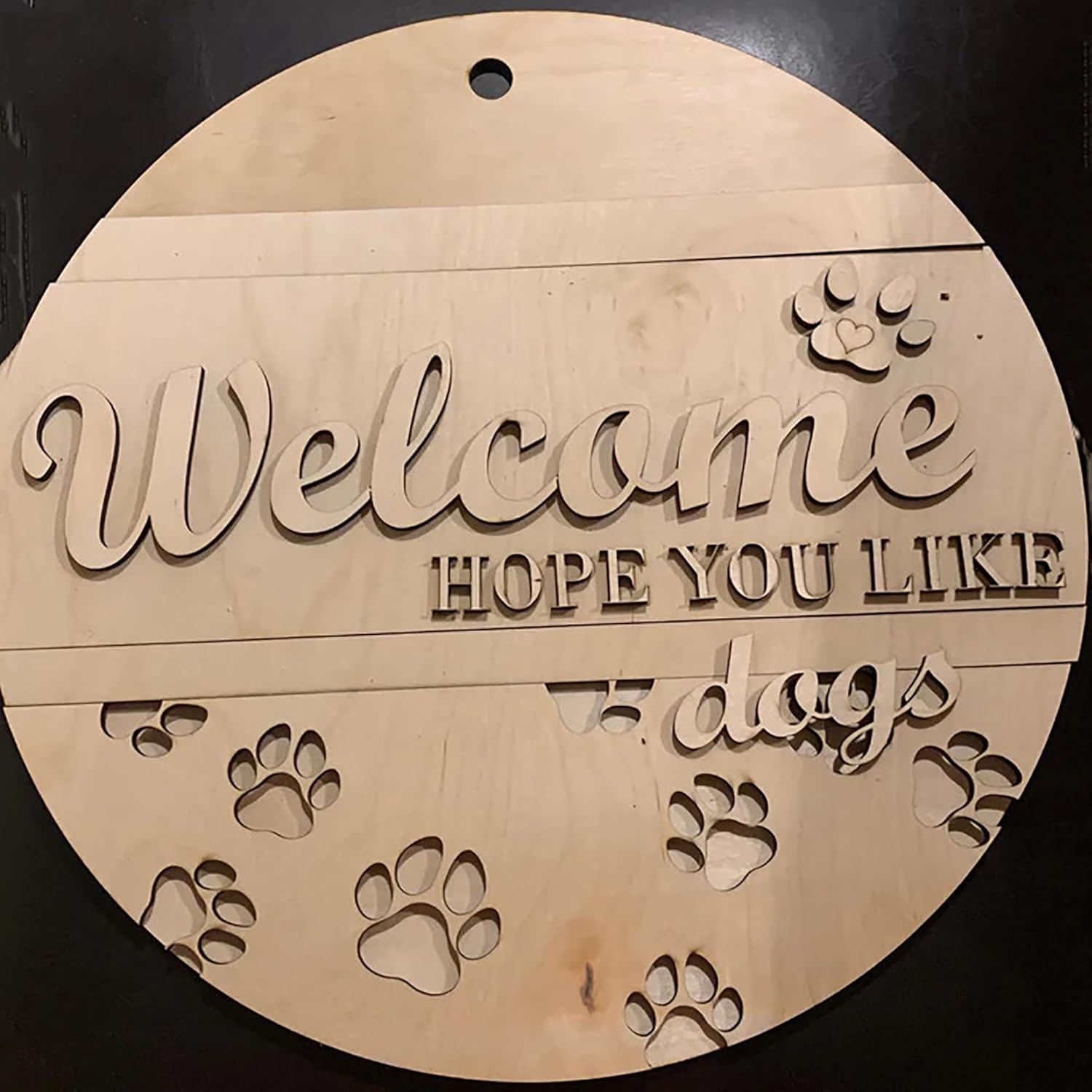 Wooden circular sign with 'Welcome hope you like dogs' text and paw prints on a black background