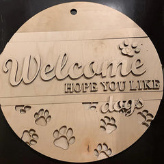 Wooden circular sign with 'Welcome hope you like dogs' text and paw prints on a black background