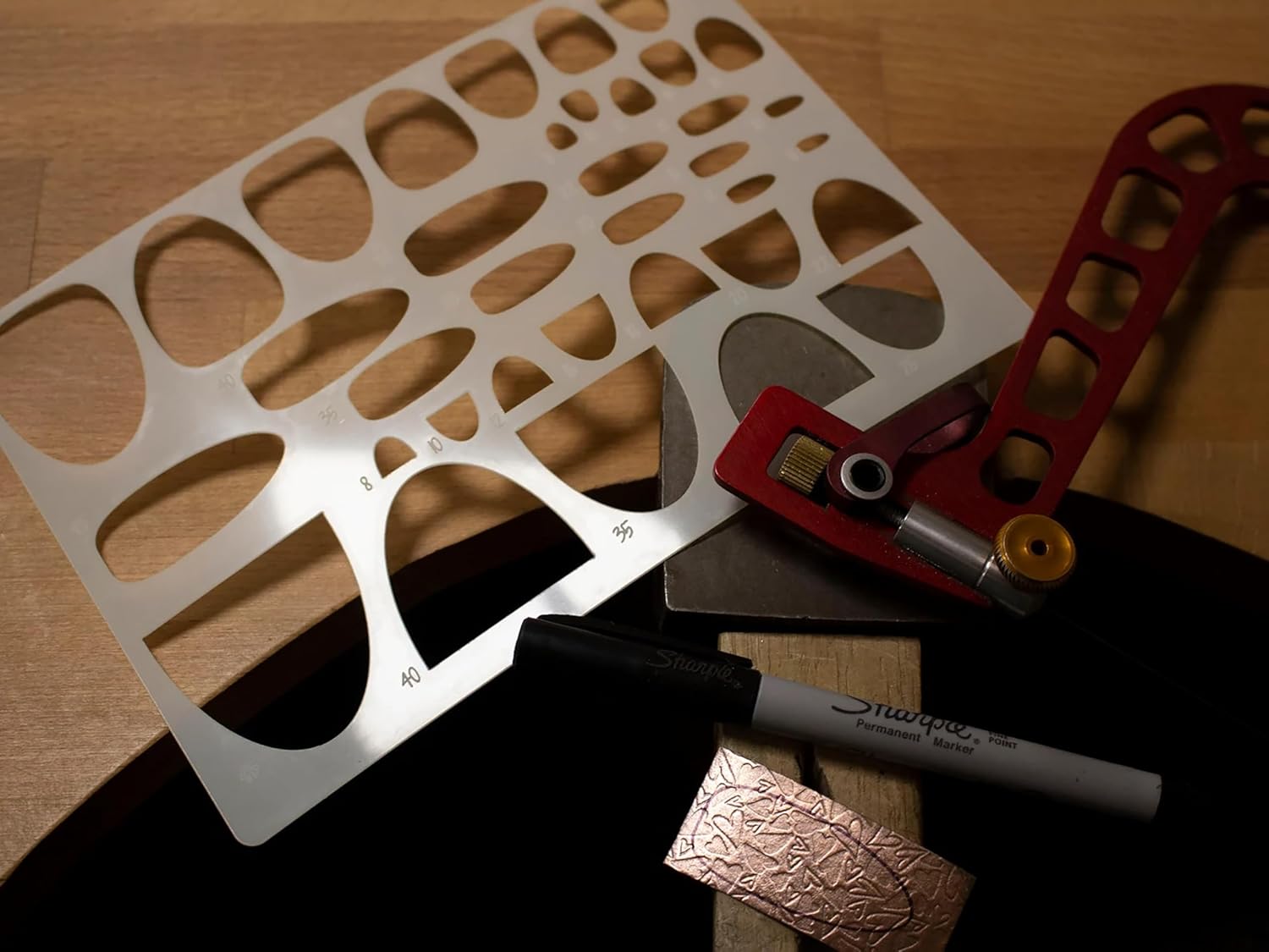 Metal template with cutouts on a wooden surface, accompanied by a marker and small metal object.