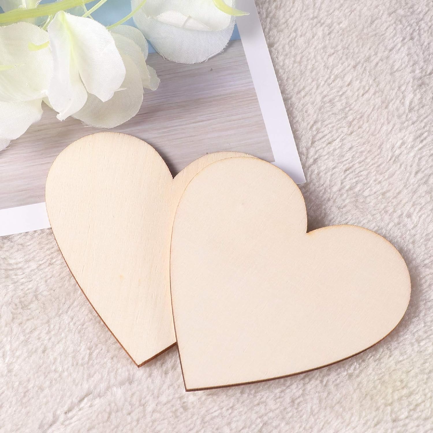 Two wooden heart-shaped objects on a textured surface with white flowers in the background.