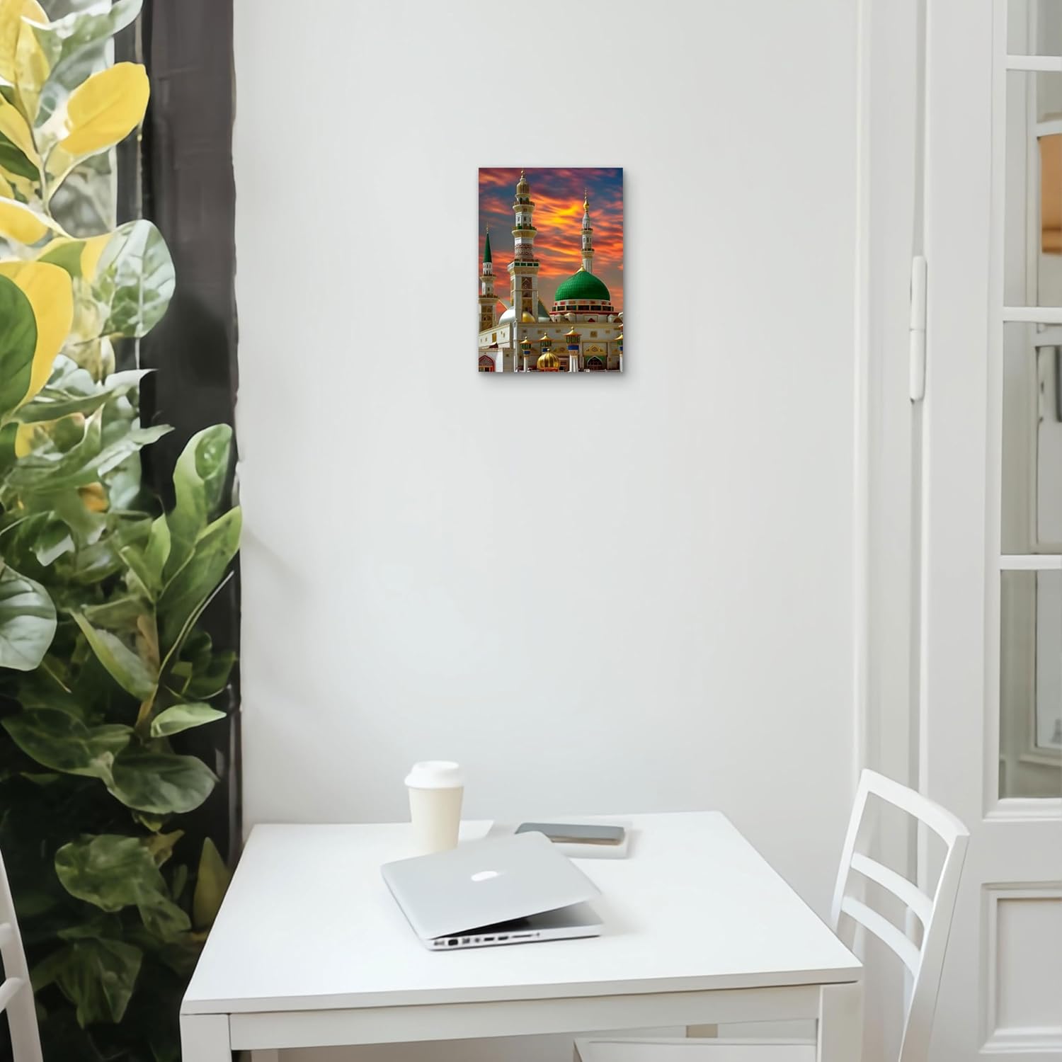 White desk with laptop, cup, and tablet next to a wall with a colorful painting of a mosque.