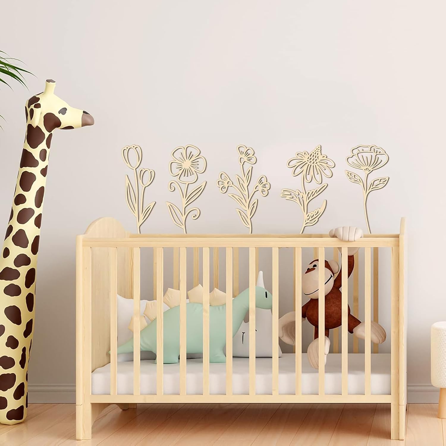 Wooden crib with stuffed animals and a tall plush giraffe in a room with floral wall art.