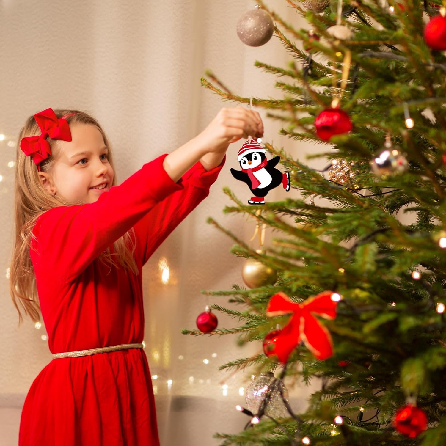 Child in a red dress decorating a Christmas tree with a penguin ornament.