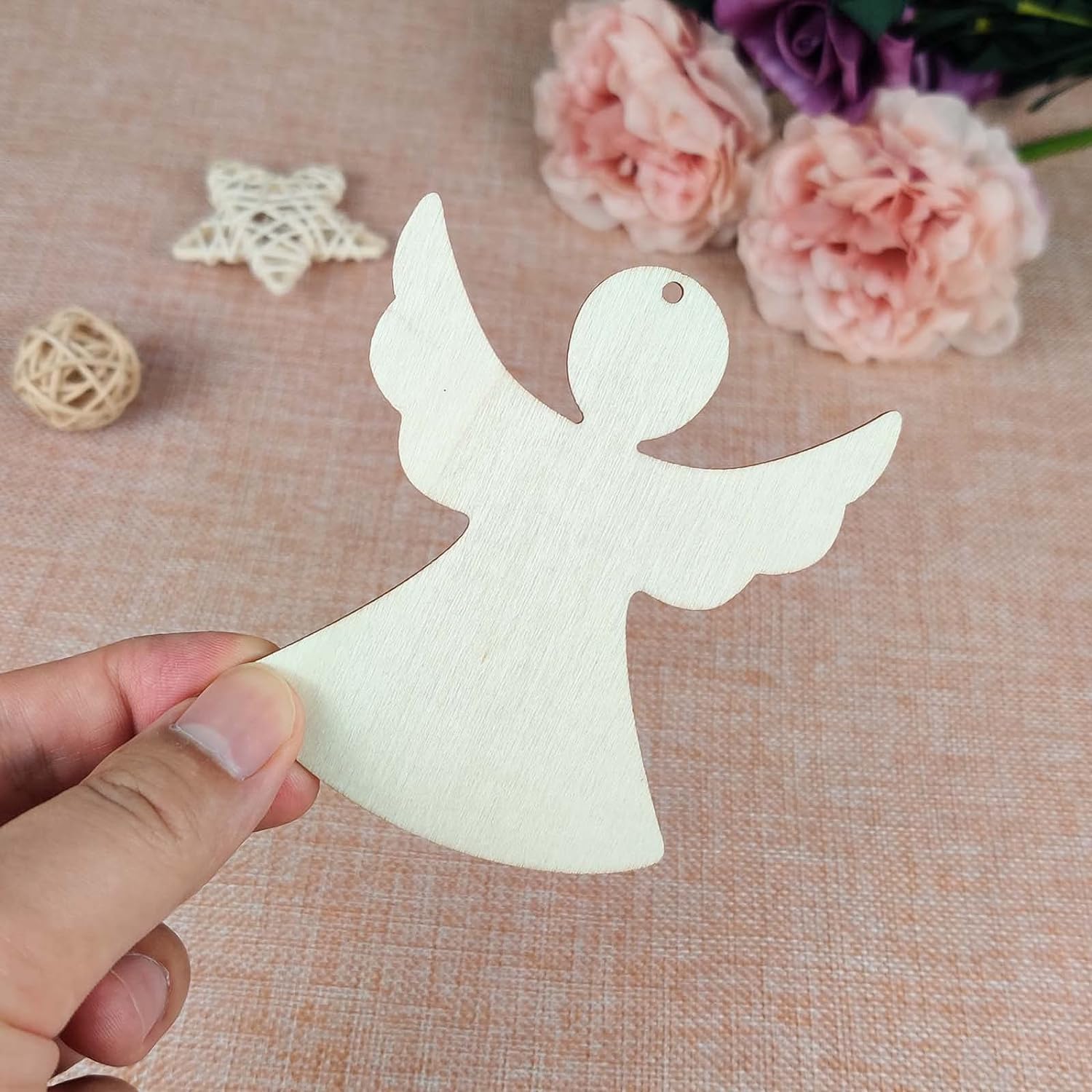 White angel cutout held by a hand on a textured surface with flowers in the background