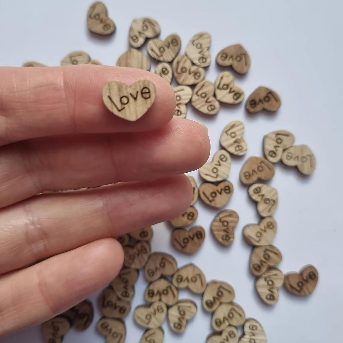 Wooden heart-shaped tokens with 'Love' and 'Bag' engraved, held by a hand on a white background.
