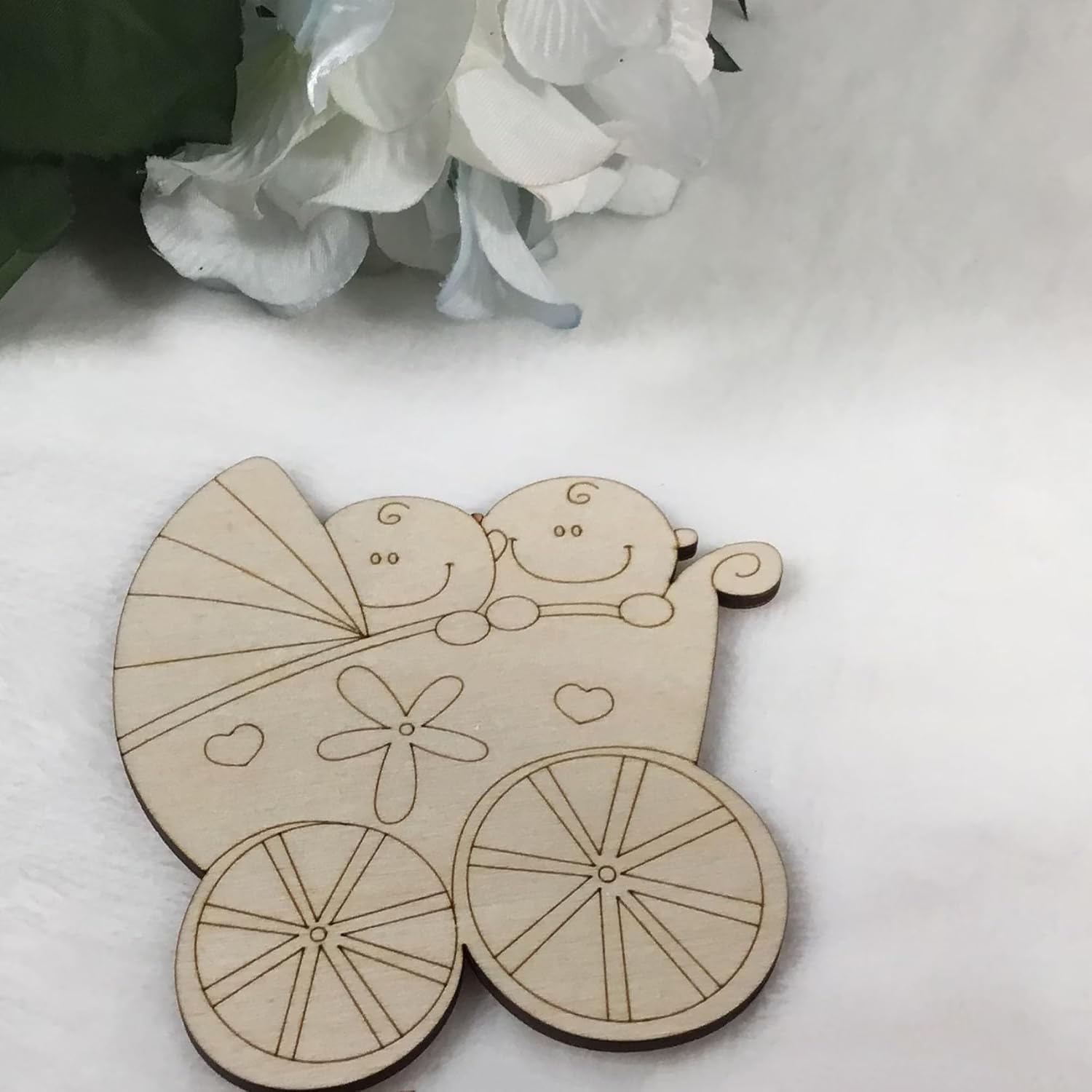 Wooden cutout of a baby carriage with two smiling babies on a white surface.