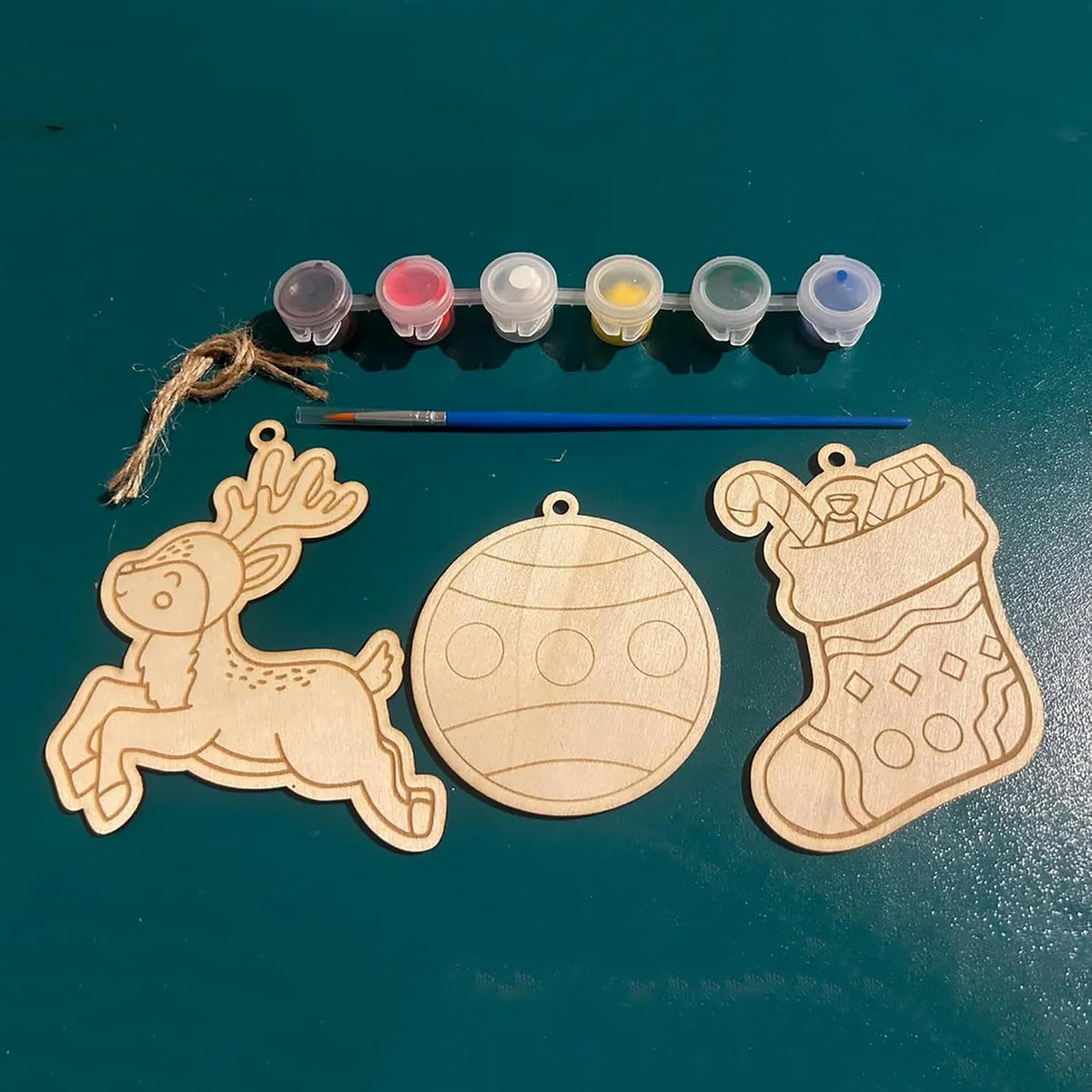 Wooden Christmas ornaments with paint supplies on a green surface