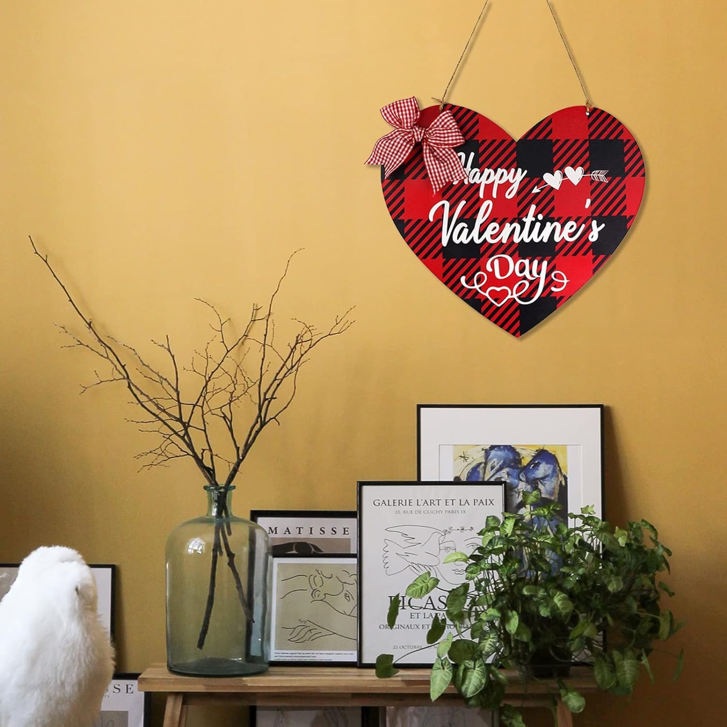 Heart-shaped Valentine's Day sign with plaid design and bow on a yellow wall.