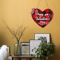 Heart-shaped Valentine's Day sign with plaid design and bow on a yellow wall.
