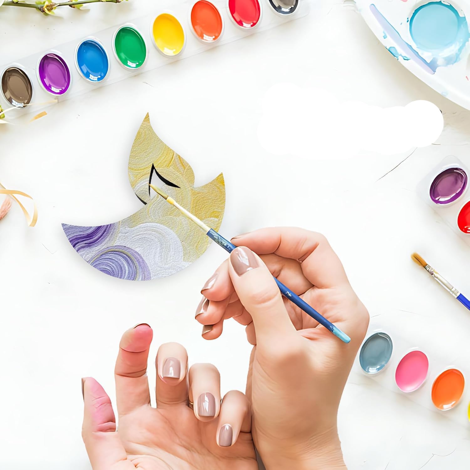 Person holding a paintbrush with watercolor paints and palettes on a white surface