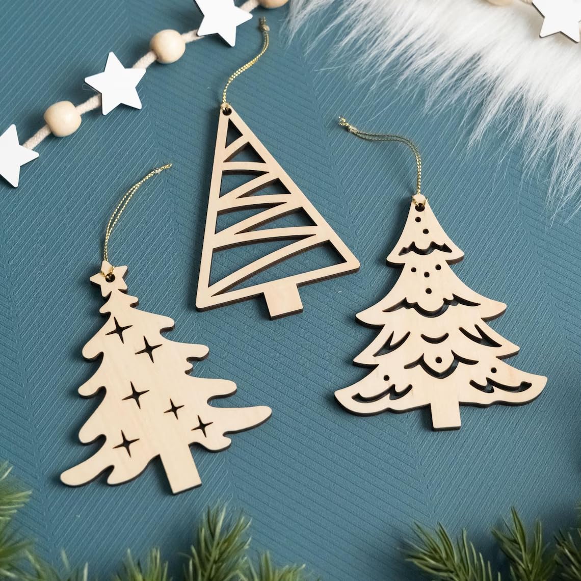 Three wooden Christmas tree ornaments on a textured blue surface with greenery around.