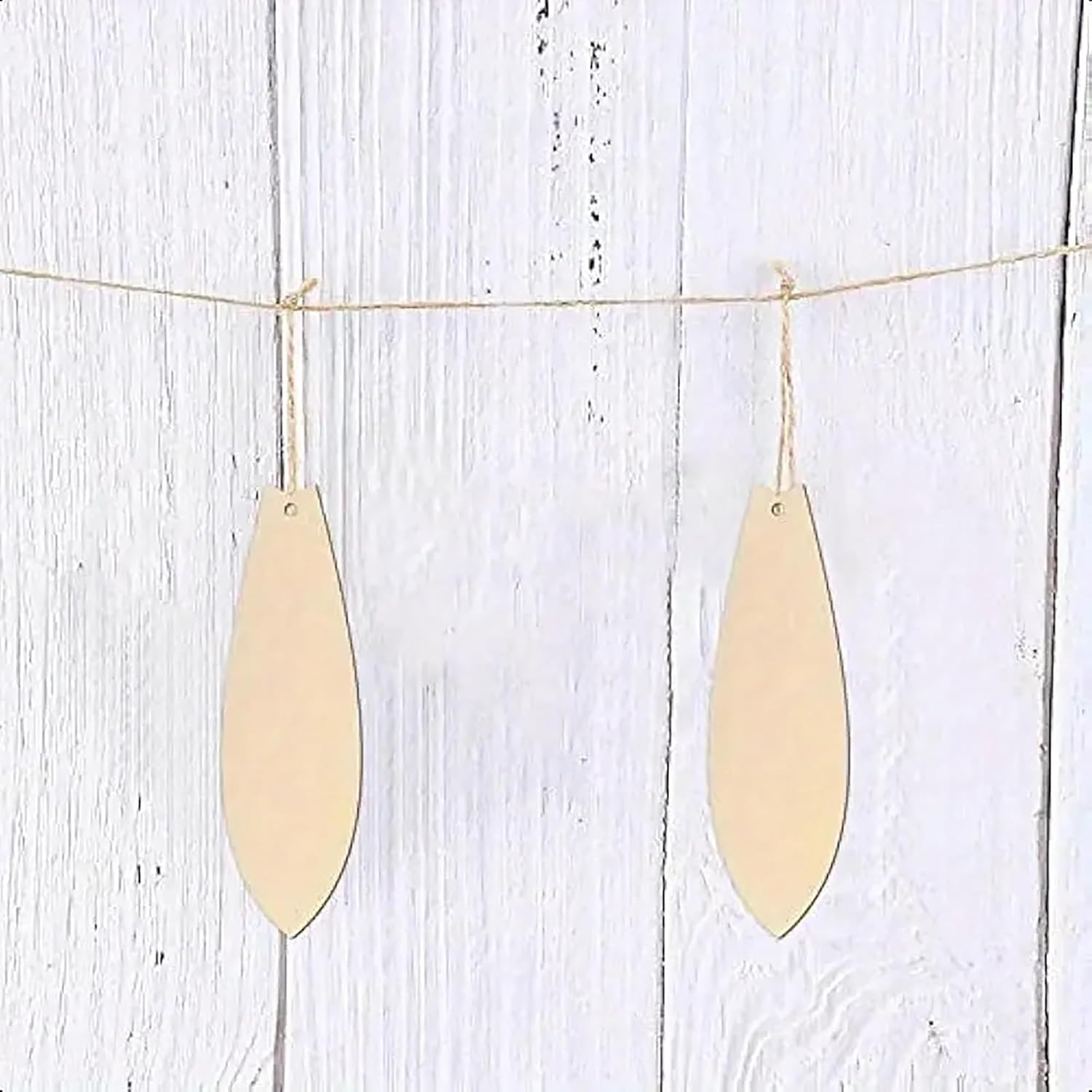 Two gold teardrop-shaped pendants hanging on a string against a light wooden background.