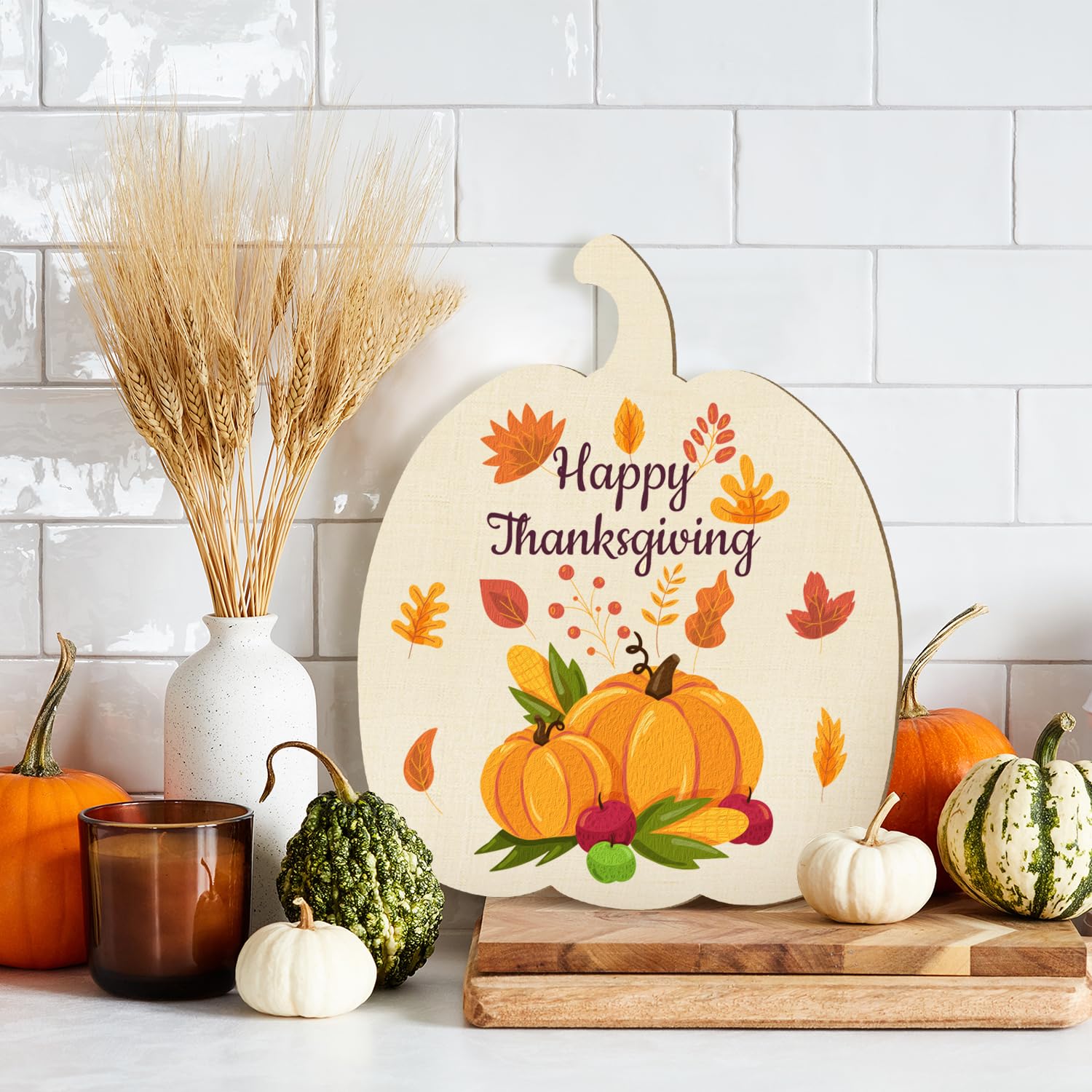 Decorative pumpkin-shaped sign with 'Happy Thanksgiving' text, surrounded by autumn-themed decor on a kitchen counter.