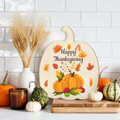 Decorative pumpkin-shaped sign with 'Happy Thanksgiving' text, surrounded by autumn-themed decor on a kitchen counter.