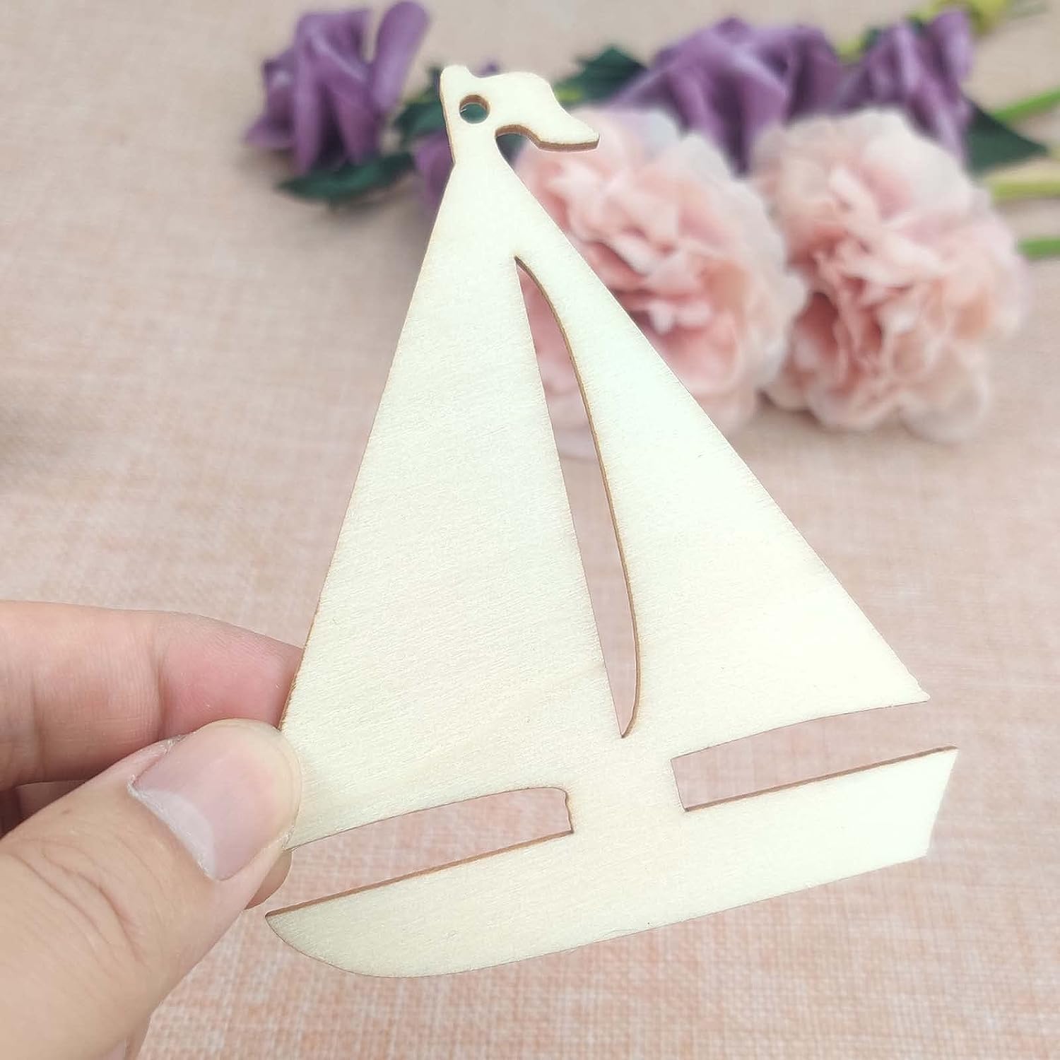 Wooden sailboat ornament held by a hand with flowers in the background