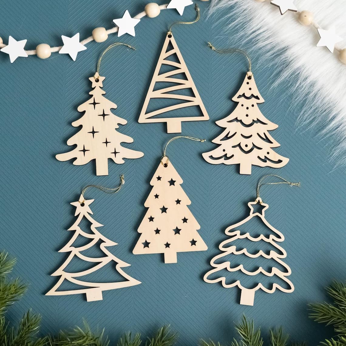 Wooden Christmas tree ornaments on a blue background with greenery around.