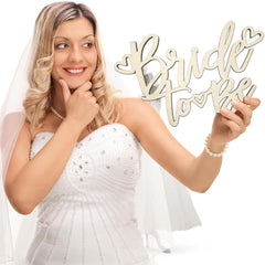 Woman in a white wedding dress holding a 'Bride to be' sign.