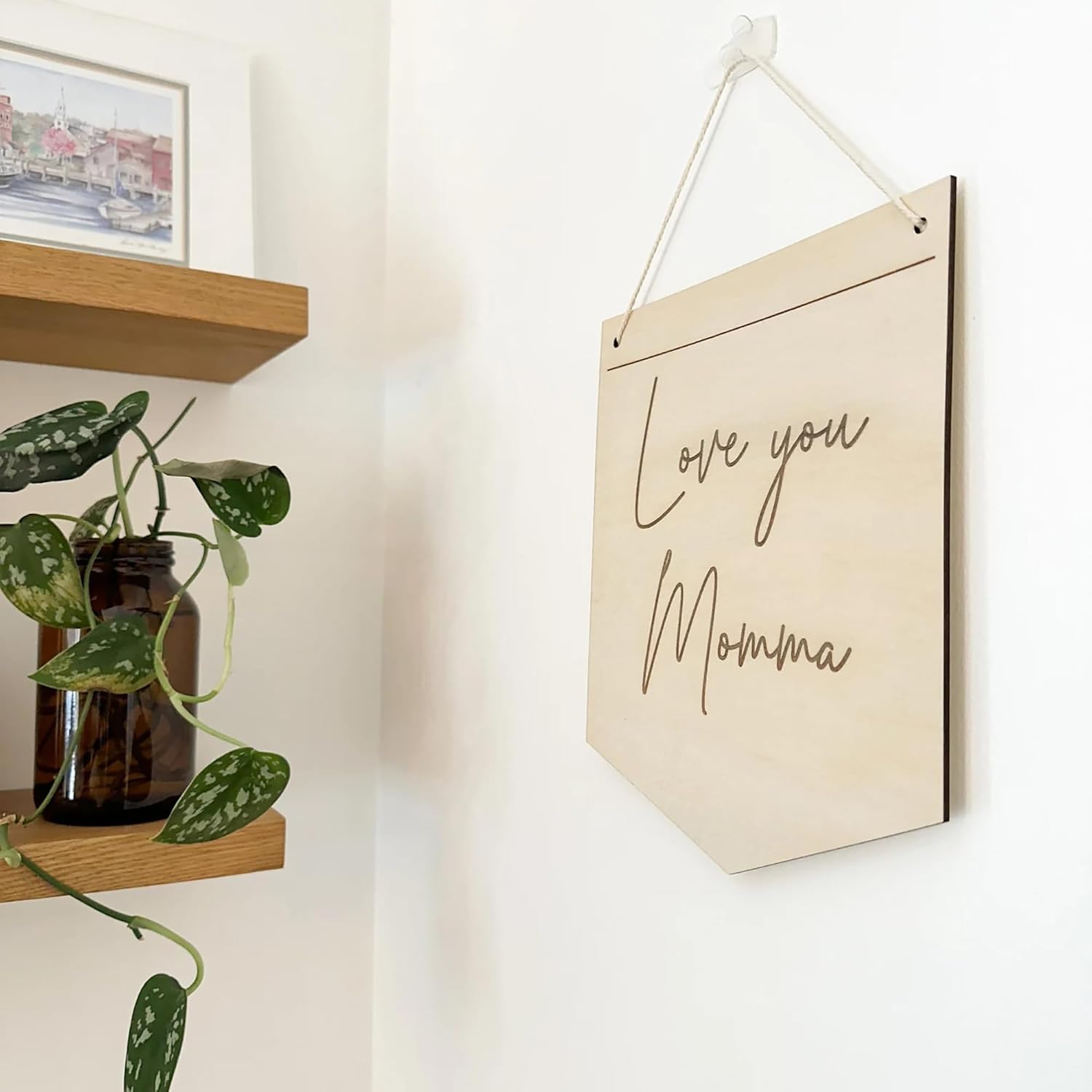 Wooden sign with 'Love you Momma' text hanging on a wall next to a plant and shelf.