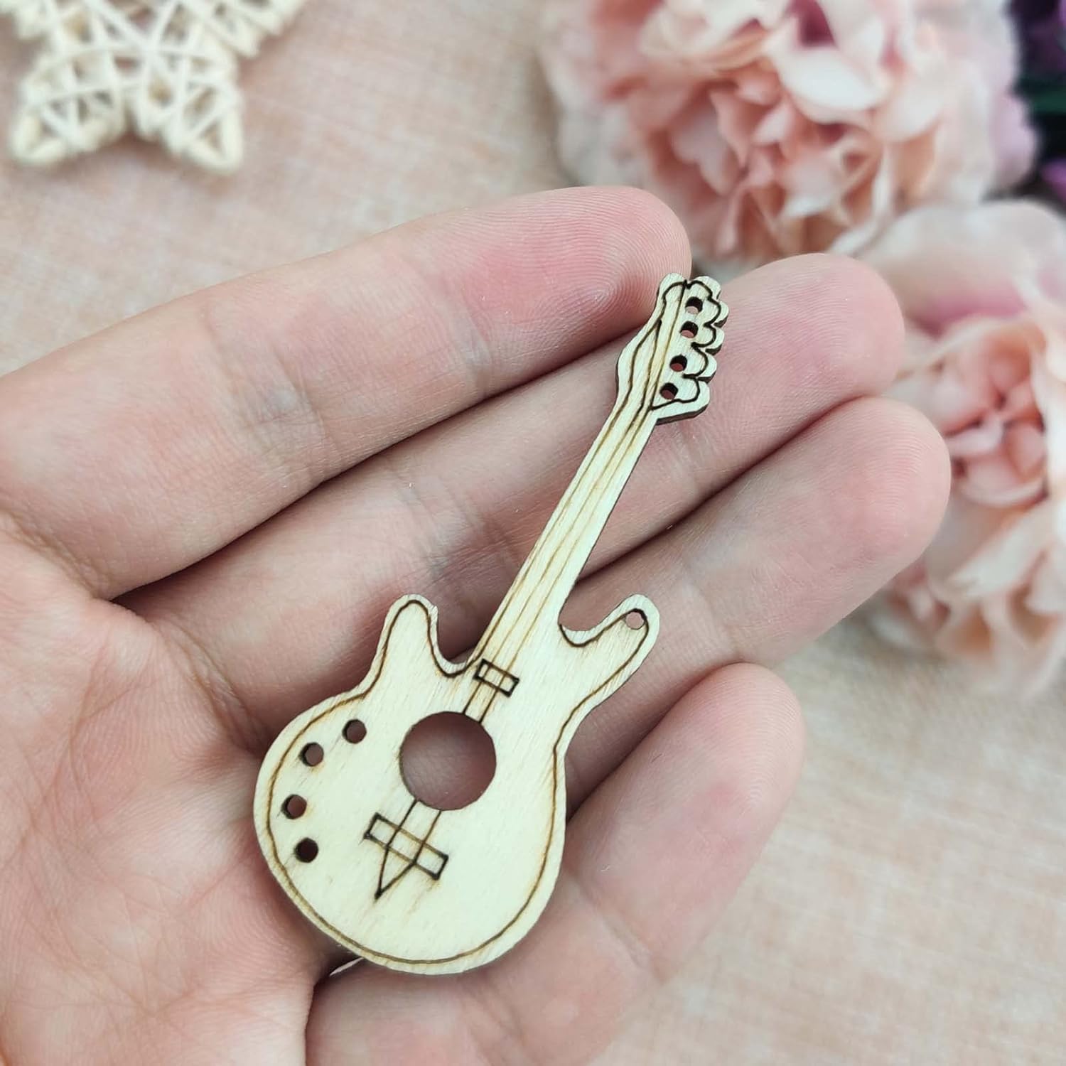 Wooden guitar-shaped pin held in a hand with a floral background
