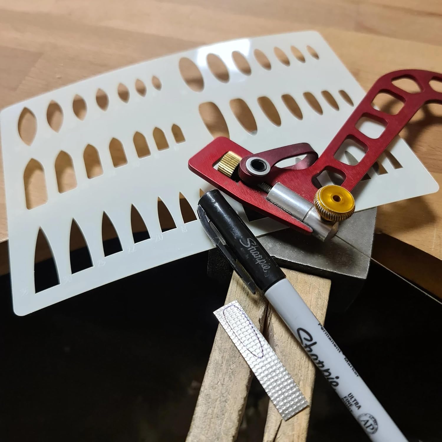 Crafting tools including a red tool, white template, and black Sharpie pen on a wooden surface.