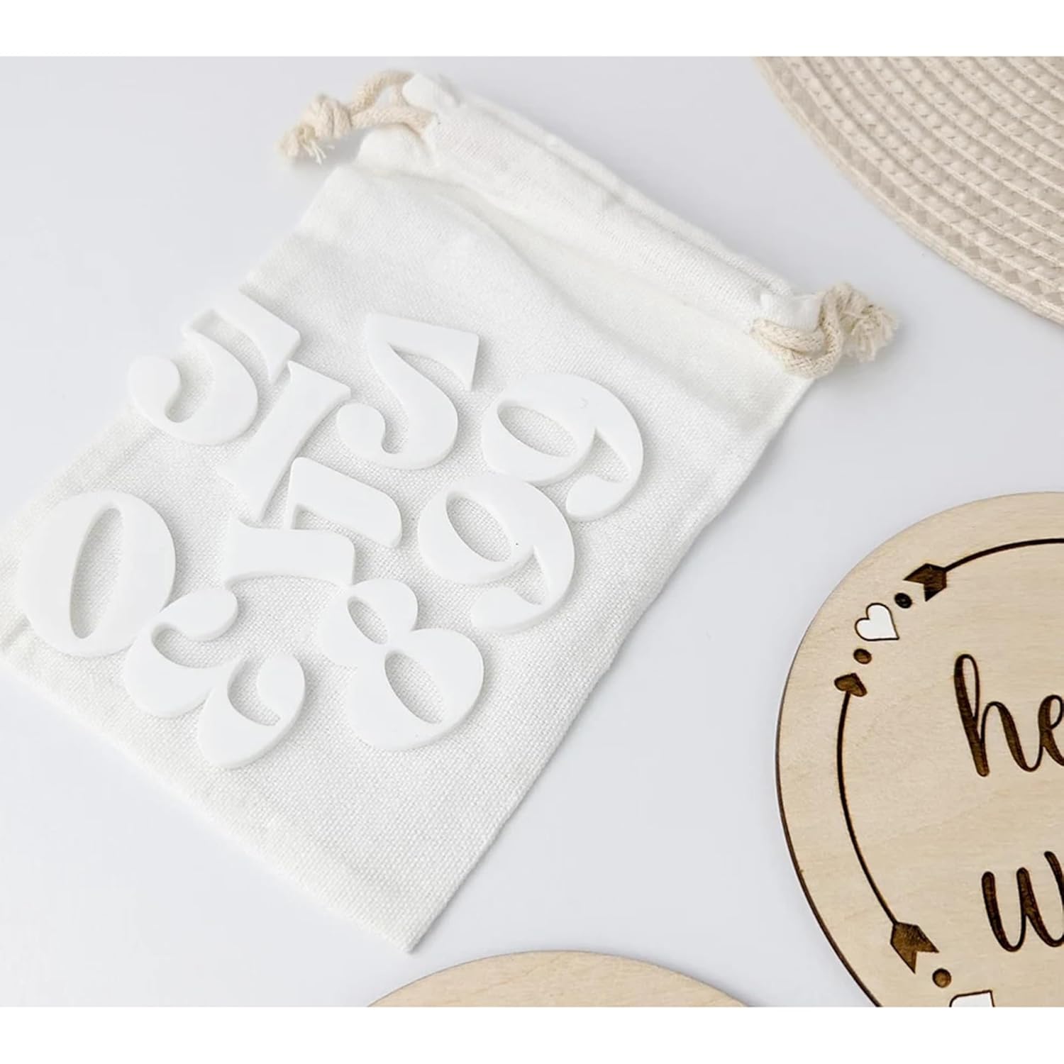 White drawstring bag with cut-out letters and a wooden sign with 'he said she said' text on a light gray background.