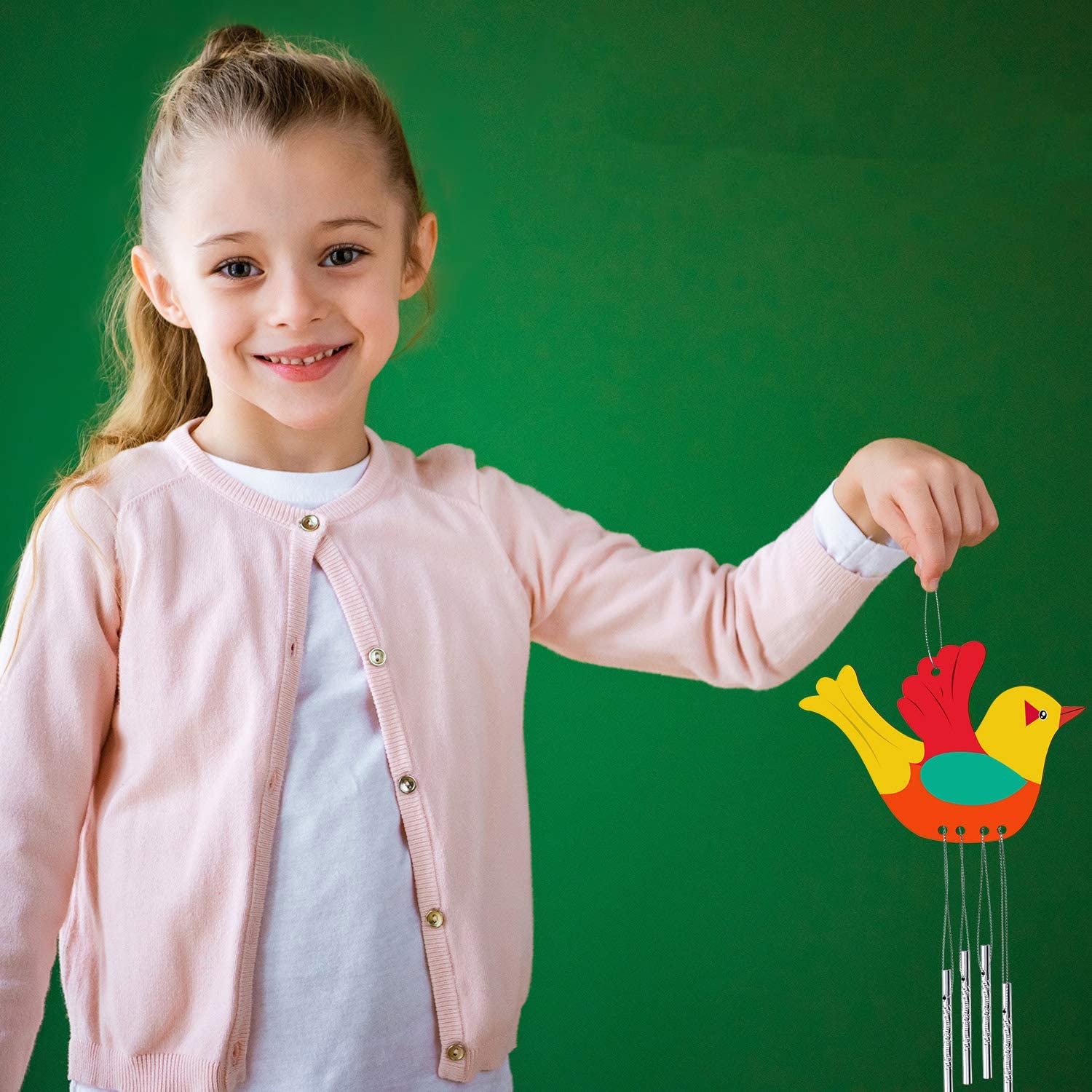 Young girl holding a colorful bird-shaped wind chime against a green background