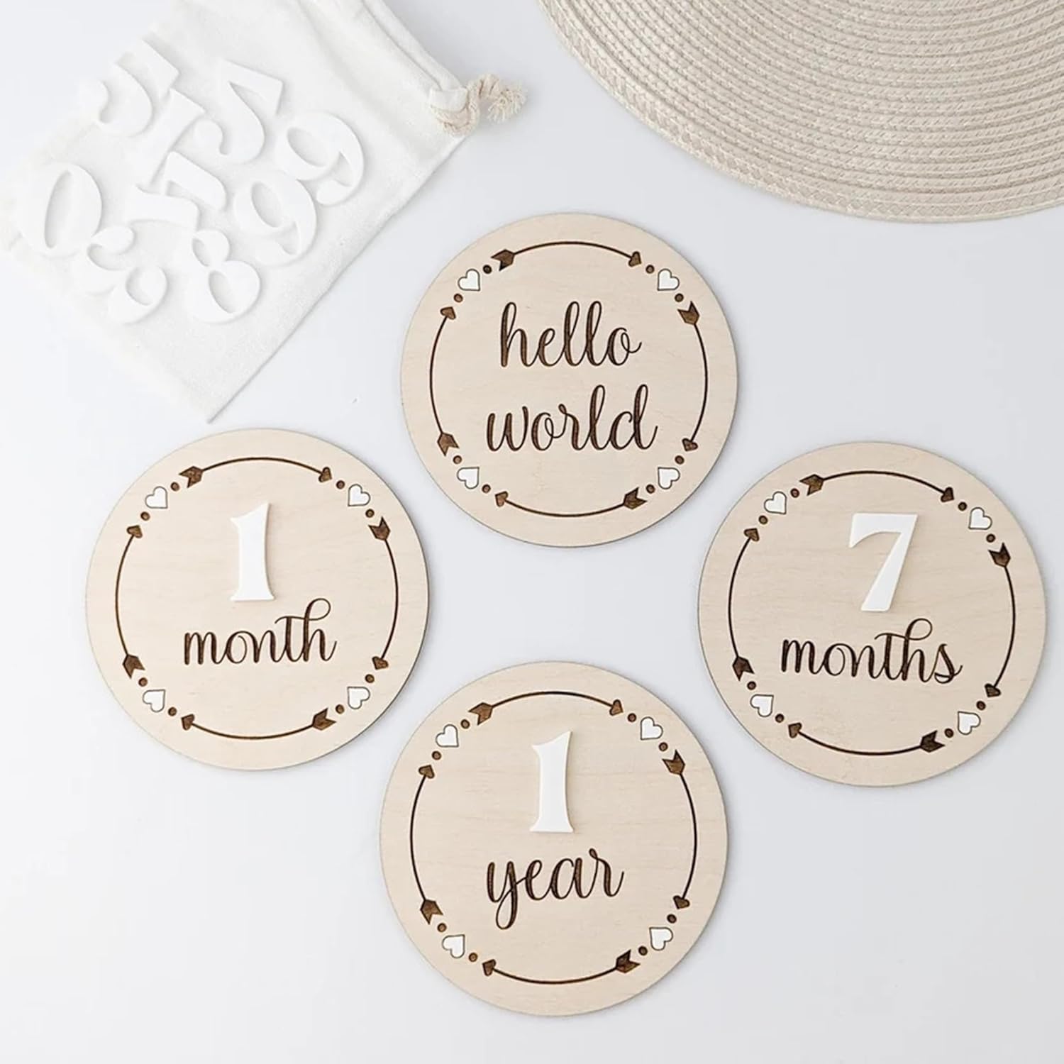 Wooden milestone discs for baby's first year with text like 'hello world', '1 month', '7 months', and '1 year' on a light background.