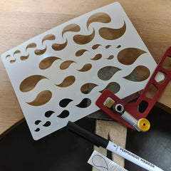 Stencil with leaf patterns, marker, and scissors on a wooden surface
