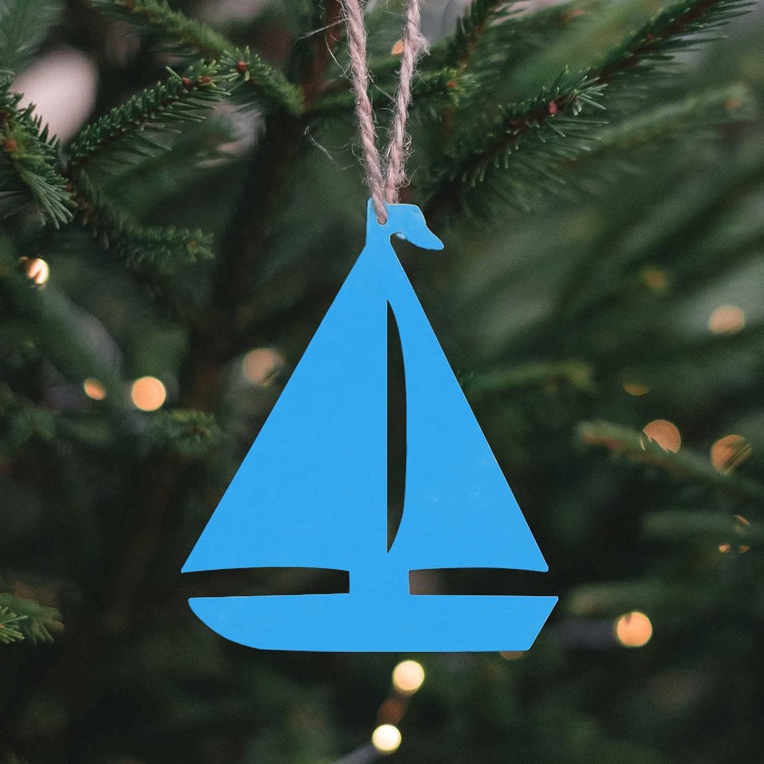 Blue sailboat ornament hanging on a Christmas tree with lights in the background