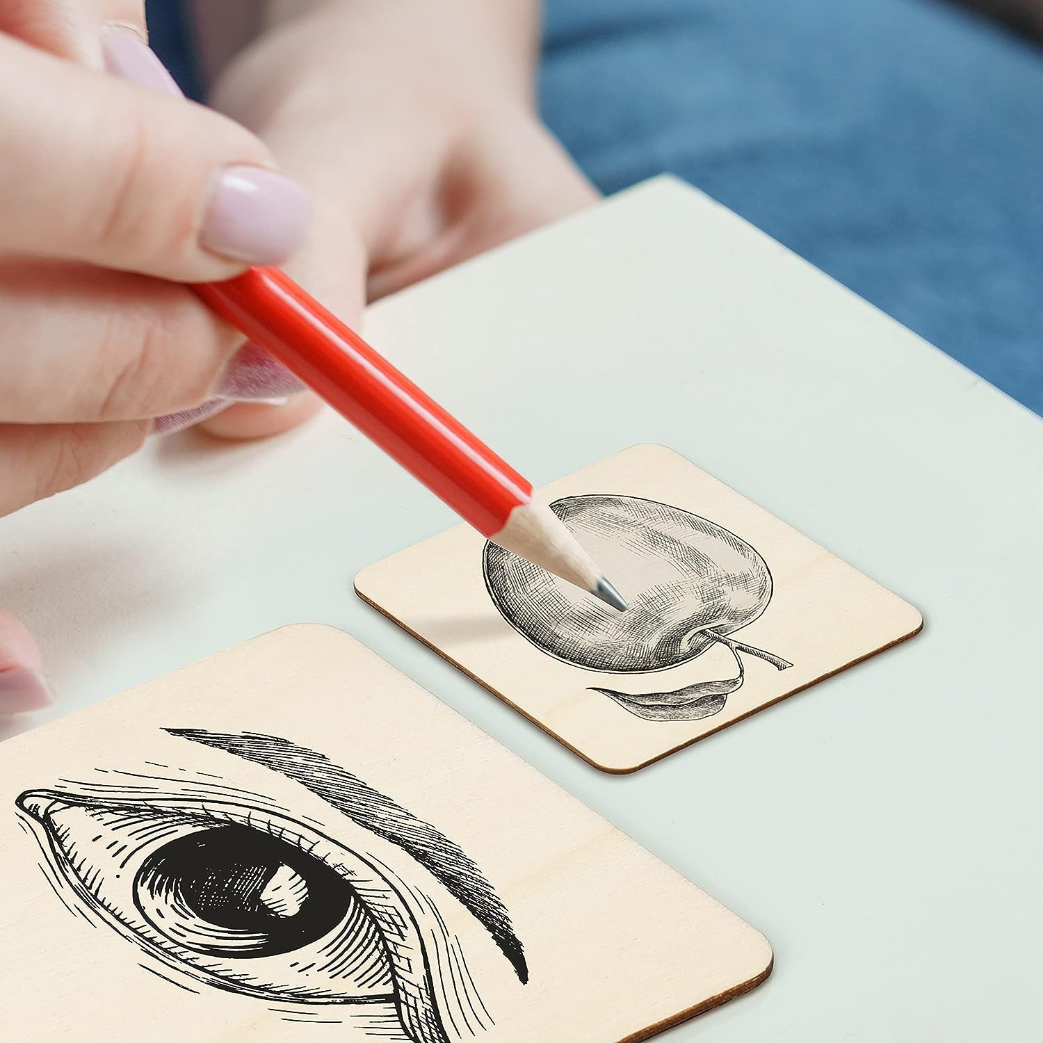 Person holding a red pencil over two wooden blocks with black ink illustrations of an eye and a peach.