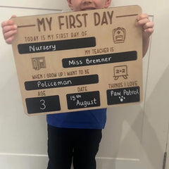 Child holding a cardboard sign for their first day of nursery with personal information.